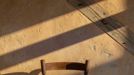 Mur chaulé ocre avec badigeon texturé inégal, poutre bois vieillie en diagonale, lumière rasante