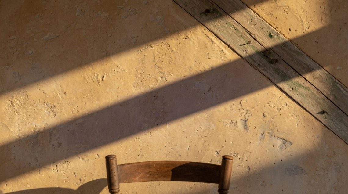Mur chaulé ocre avec badigeon texturé inégal, poutre bois vieillie en diagonale, lumière rasante